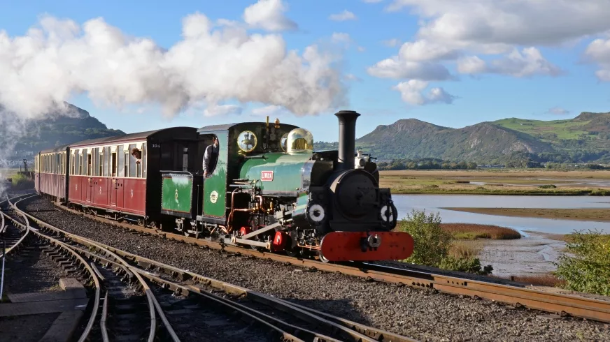 Ffestioniog Heritage Railway Steam Train in the countryside next to a lake with blue skies