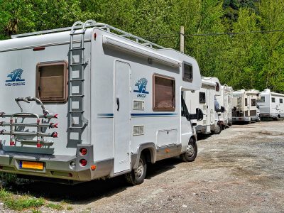 line of motorhomes parked up on a road with tall trees on the left hand side